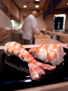 two shrimp are sitting on a plate in front of a man who is behind the counter