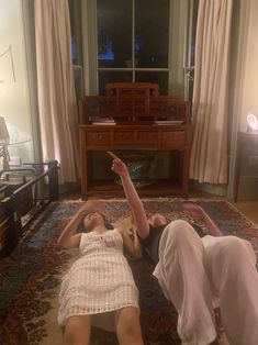 two women laying on the floor in front of a window and pointing at something off to the side