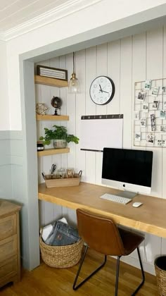 a desk with a computer on it in front of a wall mounted clock and other items