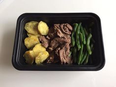 a plastic container filled with meat, potatoes and green beans on top of a white table