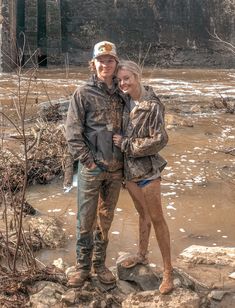 a man and woman are standing in mud near the water, posing for a photo