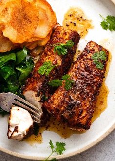 a white plate topped with meat and greens next to potato wedges on top of a table