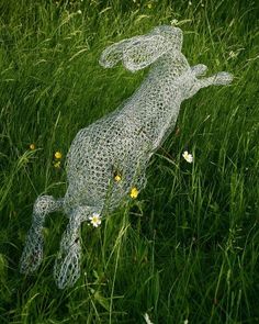 a wire sculpture of a dog laying in the grass