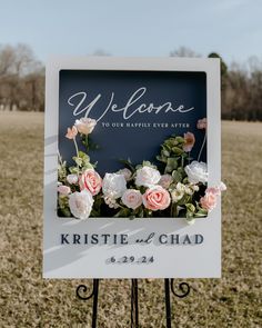 a welcome sign with flowers on it sitting in the middle of a grass covered field