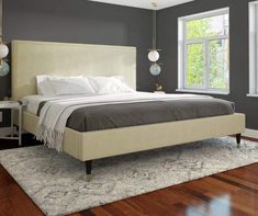 a large bed sitting on top of a wooden floor next to a white dresser and window