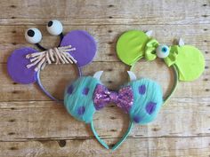 three mickey mouse ears with purple and green hair are on a wooden table next to two eyes