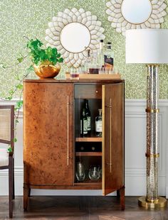 a cabinet with wine bottles and glasses on it in front of a wallpapered wall