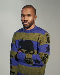 a man in a blue and green sweater is looking at the camera with his hands on his hips