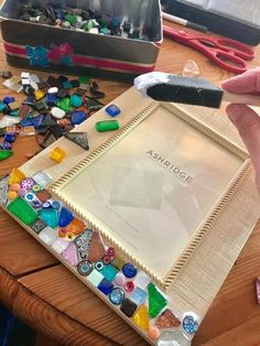 a person is holding a piece of glass in front of a picture frame that has been made out of different colored glass beads