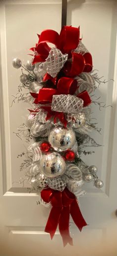 a red and silver christmas tree hanging on the front door with balls, bows and baubles