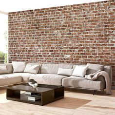 a living room with a large sectional couch and coffee table in front of a brick wall