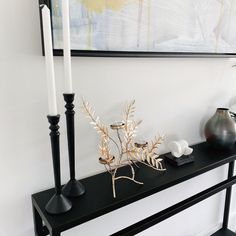 a black shelf with two candles and some plants on it next to a white wall