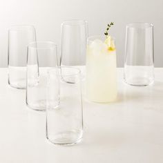 several glasses and a pitcher are lined up on a table with lemon wedges in them