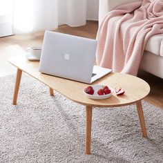 a table with a laptop and bowl of fruit on it in front of a couch