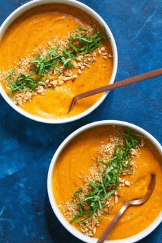 two bowls of carrot soup on a blue surface