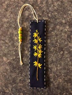 an embroidered bookmark with yellow flowers on blue fabric and white stitching hanging from a string