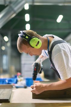 a young man wearing headphones and working on a piece of wood with a drill