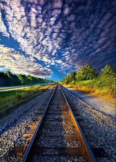 an empty train track with the sky in the background and trees on both sides, under a cloudy blue sky