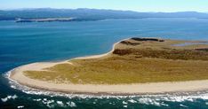 an island in the middle of the ocean with sand and grass on it's shore