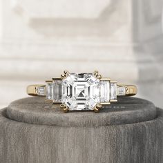 an emerald cut diamond ring with baguettes on the band and side stones in yellow gold