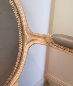 the back of a chair that is upholstered with beaded trim and an oval mirror