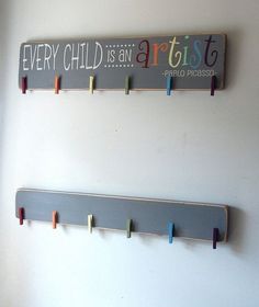 two wooden pegs are hanging on the wall next to a sign that says every child is an artist