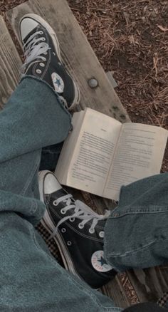 someone is reading a book while sitting on a bench with their legs crossed and feet propped up