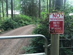 a red and white no trespassing sign next to a forest trail with trees