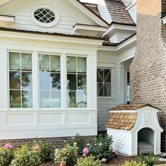 a dog house is shown in front of some flowers and bushes on the side of a house