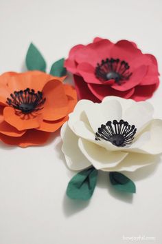 three paper flowers with green leaves and red, orange, and white petals on them