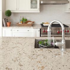 a kitchen with marble counter tops and white cabinets, an island style sink and stainless steel appliances