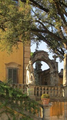 an old building with statues on the steps and trees growing up to it's sides