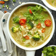 two bowls of soup with broccoli, tomatoes and other vegetables on the side