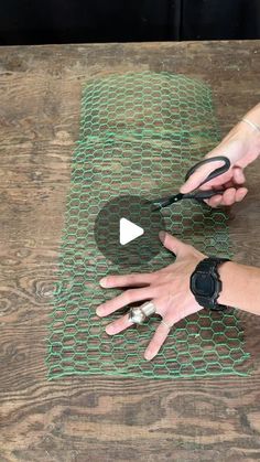 a person is cutting up some material on a wooden table with scissors and wire attached to it