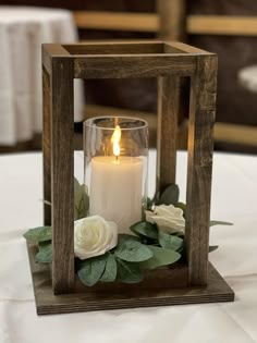 a candle that is sitting inside of a wooden box with flowers on the side and greenery around it