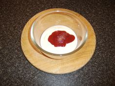 a wooden plate topped with a small bowl filled with sauce on top of a table