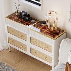 a white dresser with drawers and gold trimmings in a room next to a window