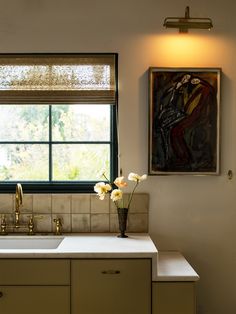 a kitchen sink under a window in front of a painting and vase with flowers on it