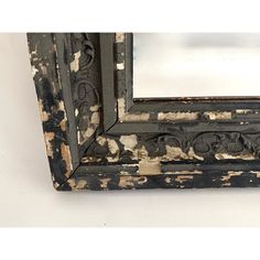 an old mirror with peeling paint on the edges and wood trimmings, sitting against a white wall