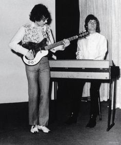 an old black and white photo of two people playing guitar in front of a piano