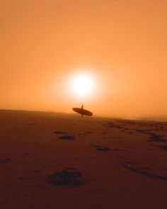 a person holding a surfboard on top of a sandy beach under a bright orange sky