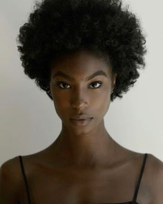 a woman with an afro looks at the camera while wearing a tank top and black bra