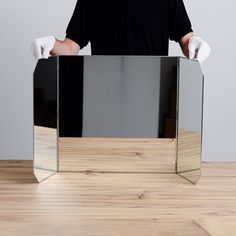 a man in black shirt and white gloves holding up a mirror on top of a wooden table