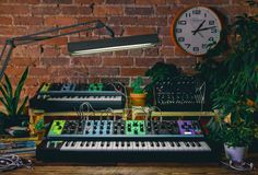 an electronic keyboard sitting on top of a wooden table next to a clock and plants