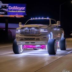 a white truck with big wheels on the road at night time in front of a neon sign