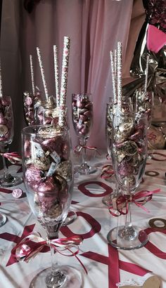 several wine glasses filled with candy and candies sitting on a table covered in pink ribbon