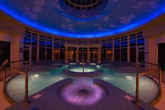 a large indoor swimming pool with blue lighting on the ceiling and sky in the background