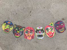 five colorful masks are lined up in a row on the ground, with faces painted on them