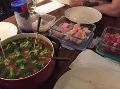 a person sitting at a table with food in bowls and plates on it, including broccoli