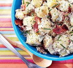 a blue bowl filled with potato salad on top of a colorful table cloth next to silverware